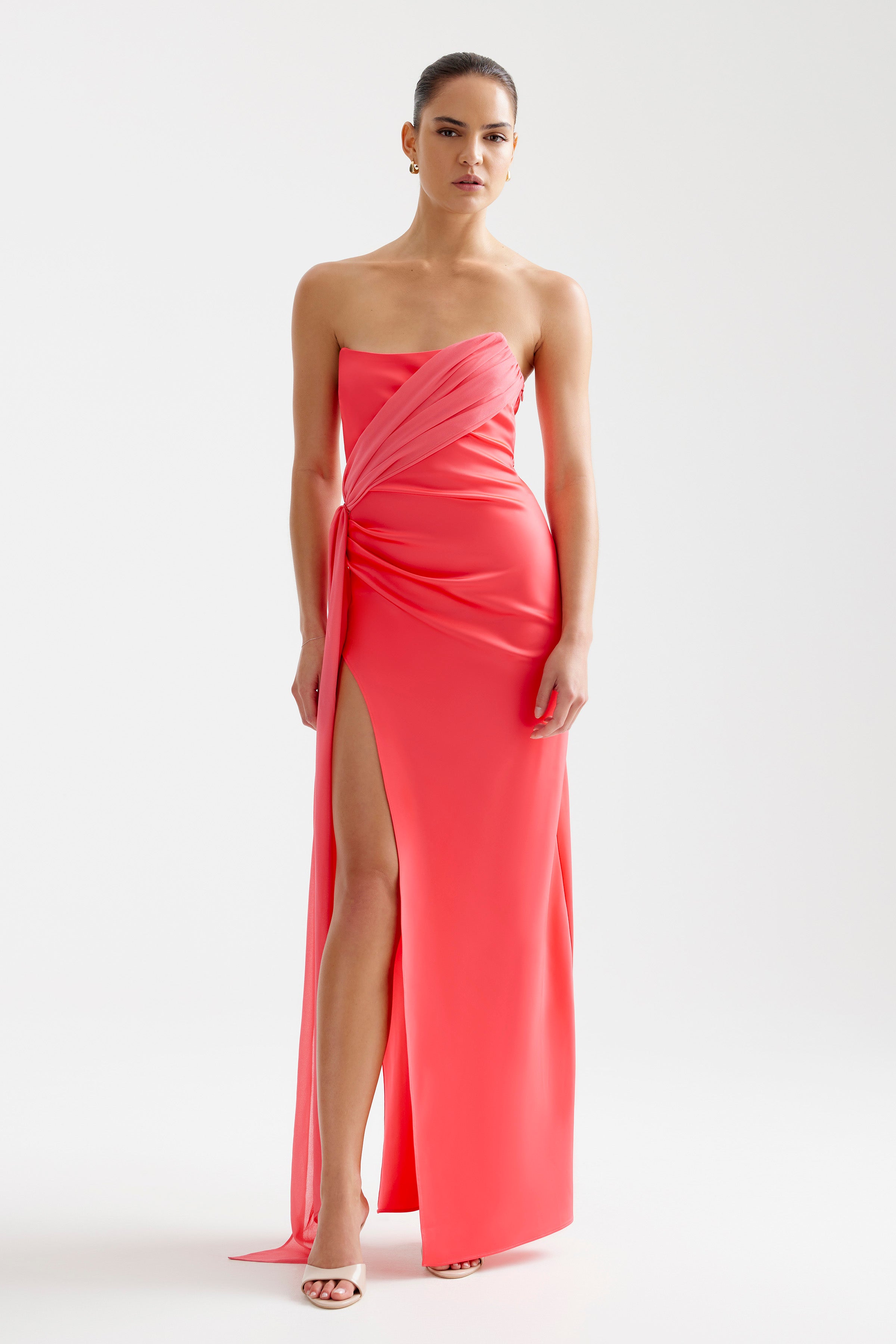 Aura Dress featuring a strapless design with draped detail and thigh-high split in vibrant coral for formal occasions by Studio Lexi