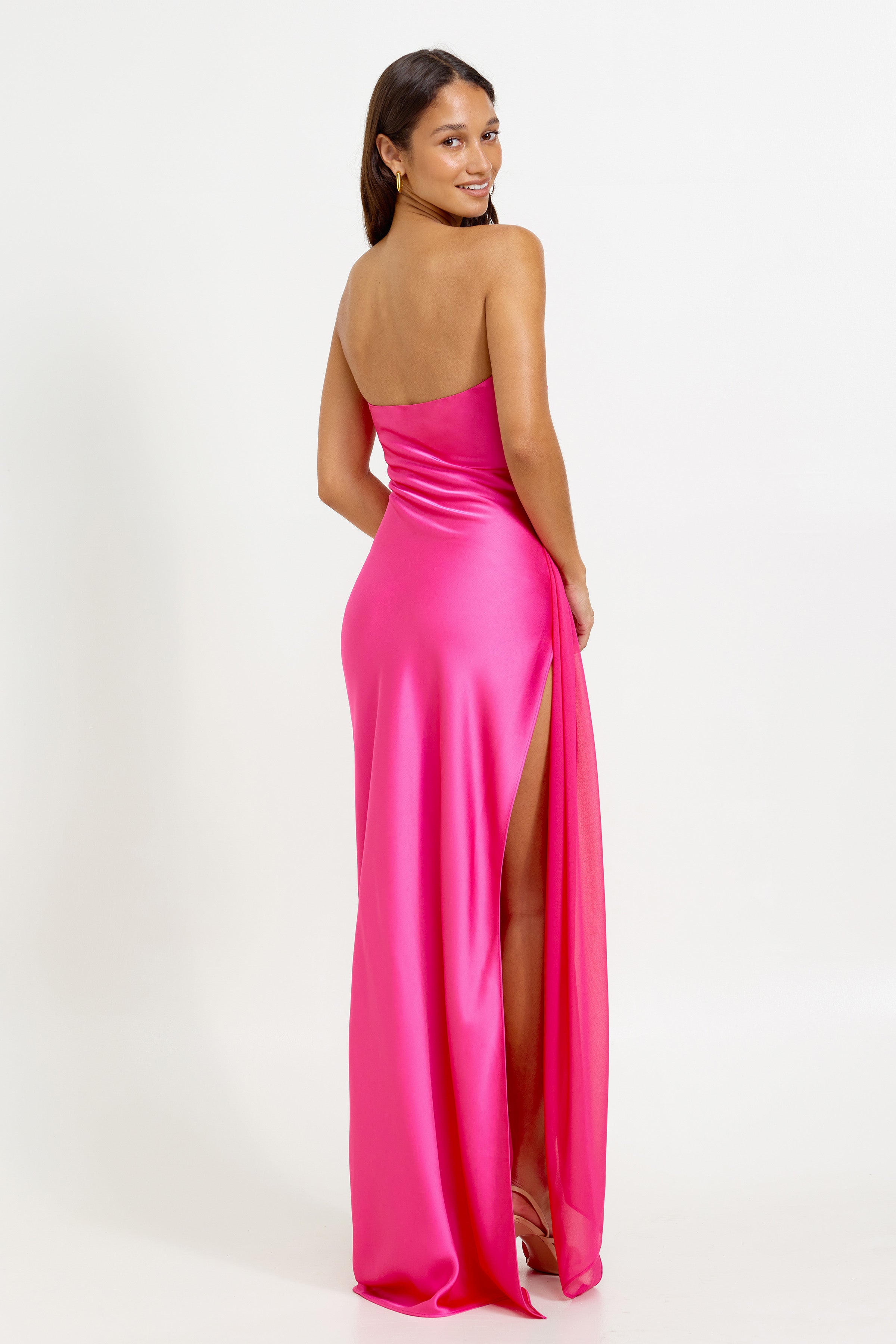 Aura Dress featuring a strapless backless design with a high slit in vibrant hot pink for formal occasions