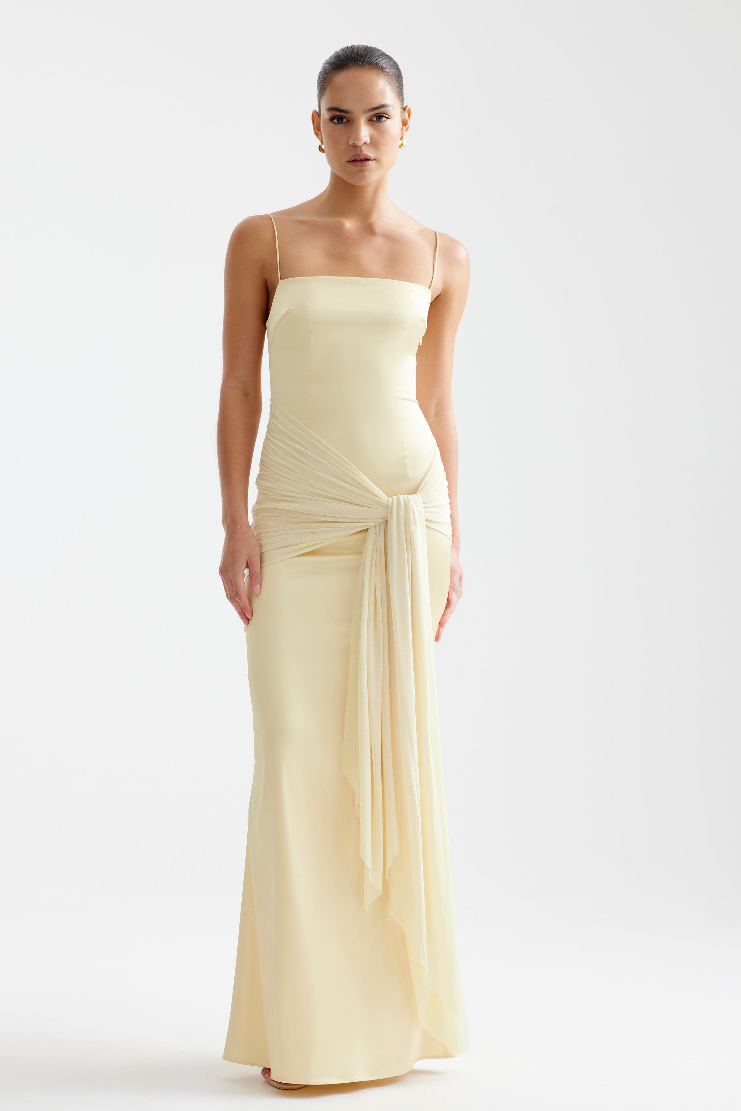 Ayla Dress featuring a sleek fitted silhouette with thin straps and draped sash detail in soft limoncello tone