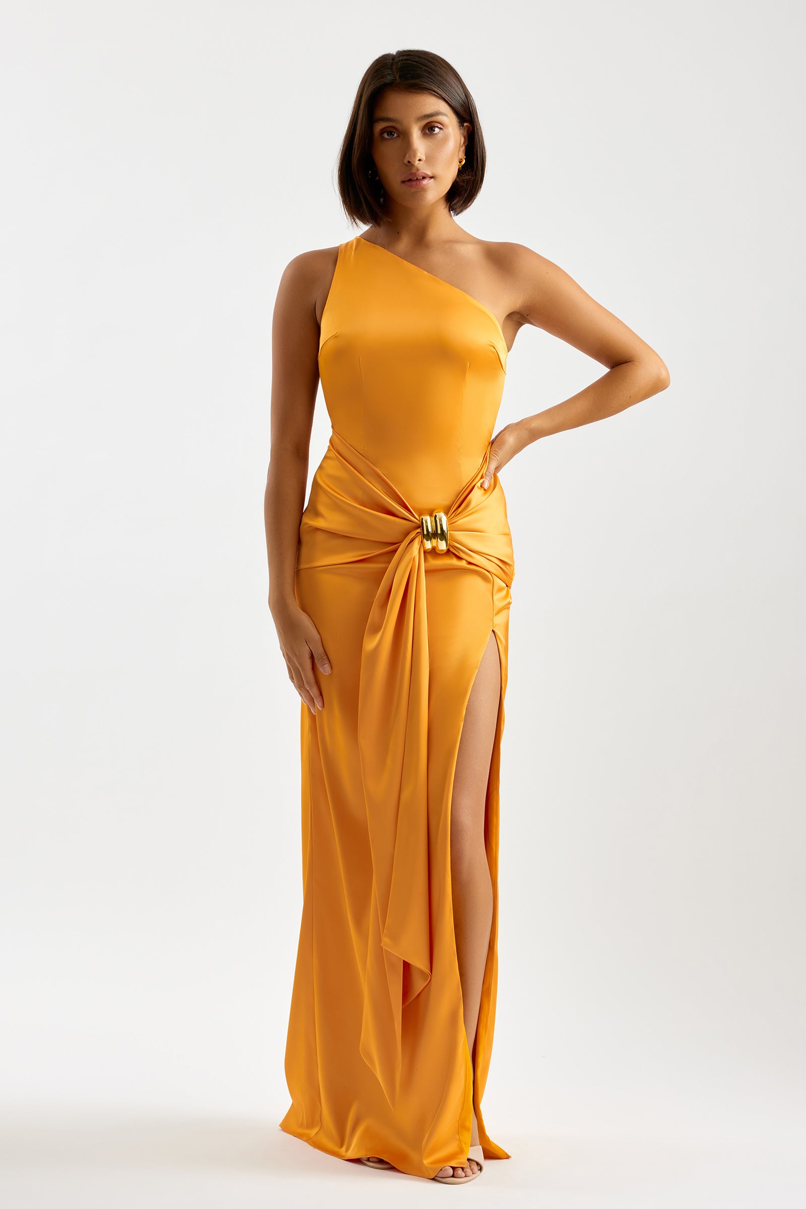 Clea Dress with one-shoulder neckline, side split, and draped waist detail in orange for formal and wedding occasions by Studio Lexi