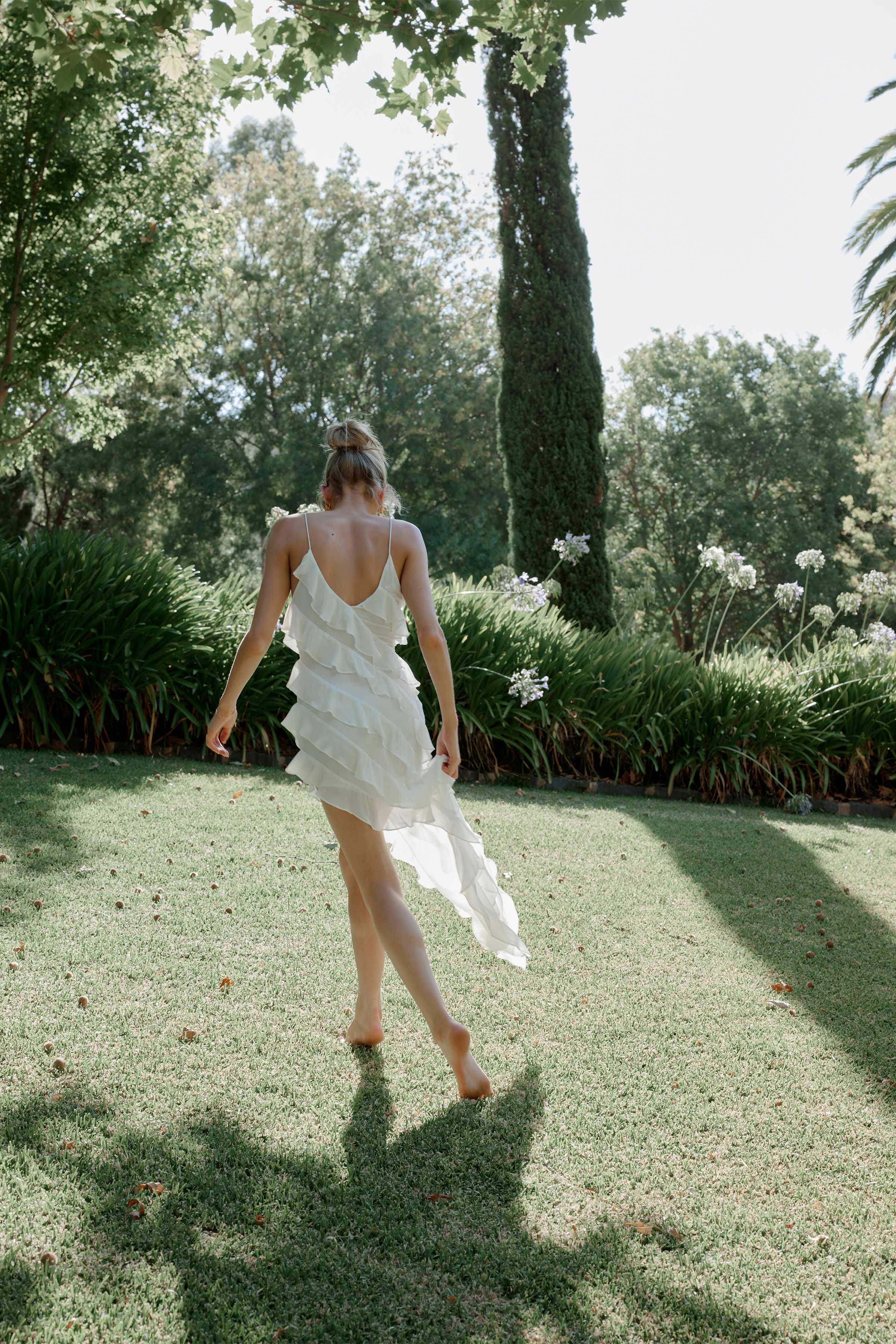 Etienne Dress featuring layered ruffles, flowing high-low hem, and delicate straps in lightweight white fabric for elegant occasions