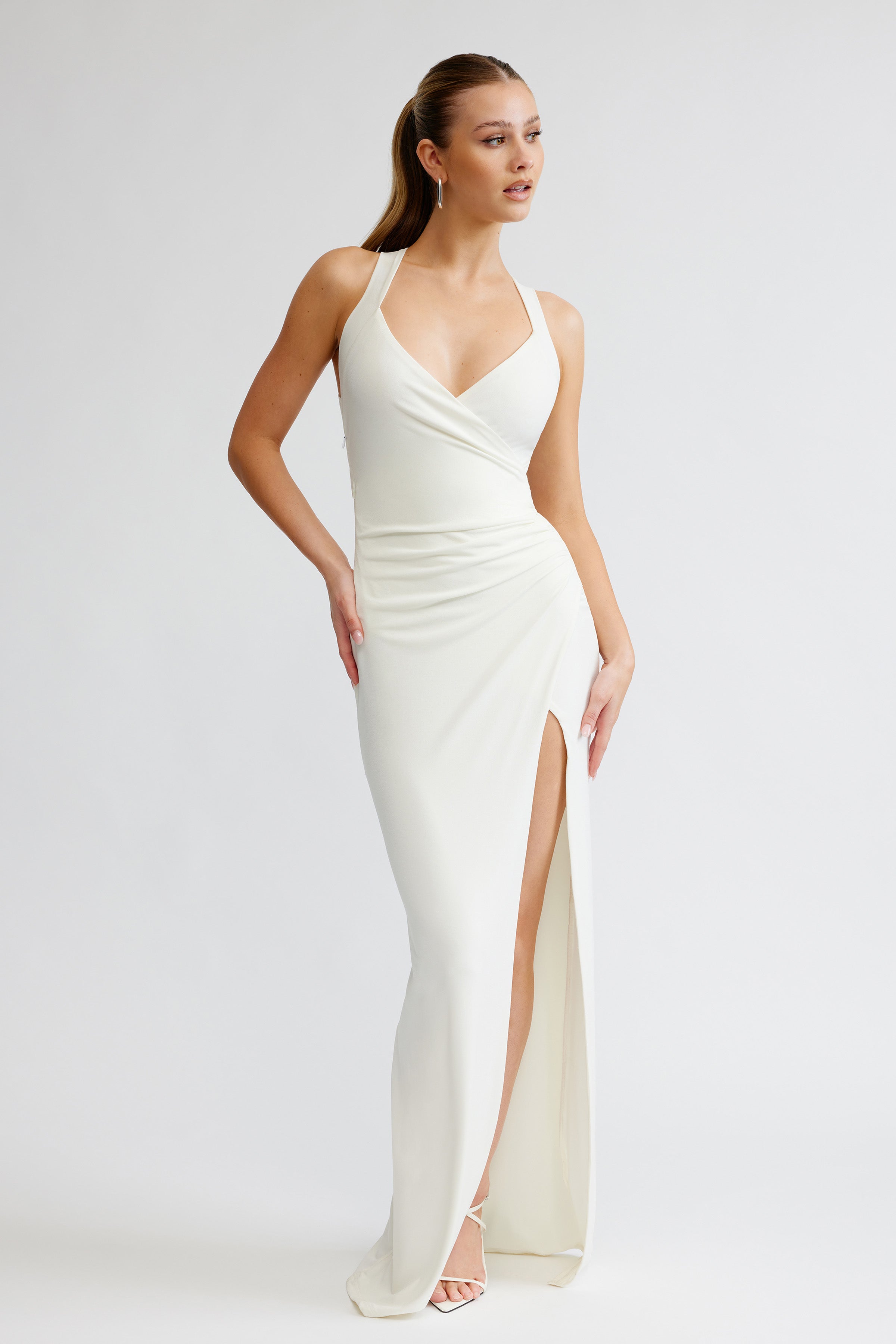 Iva Dress featuring a halter neck, ruched waist, and high slit in white for formal and bridesmaid occasions