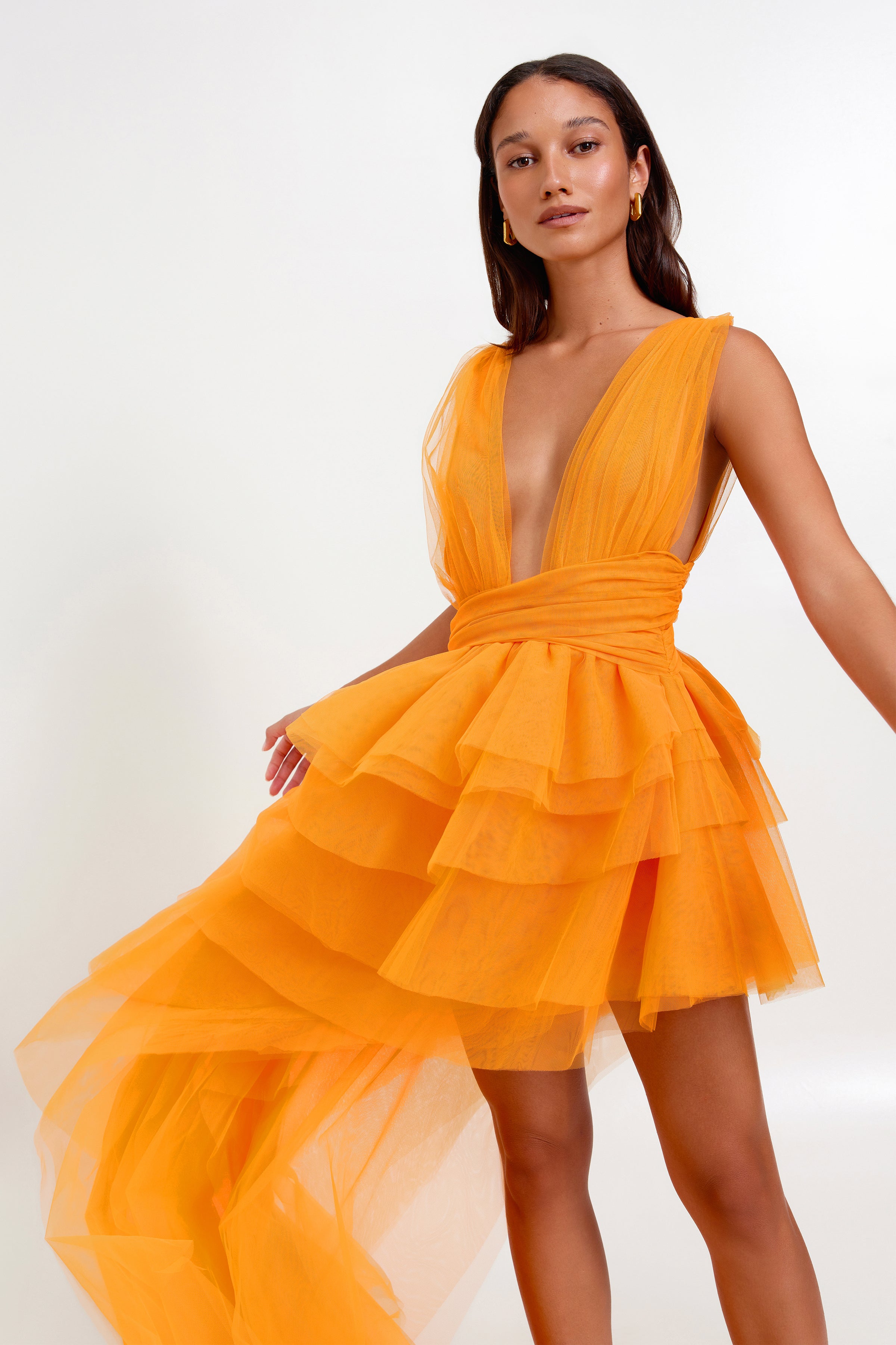 Lola Dress featuring a plunging neckline and tiered tulle skirt with a flowing small train in vibrant mango shade