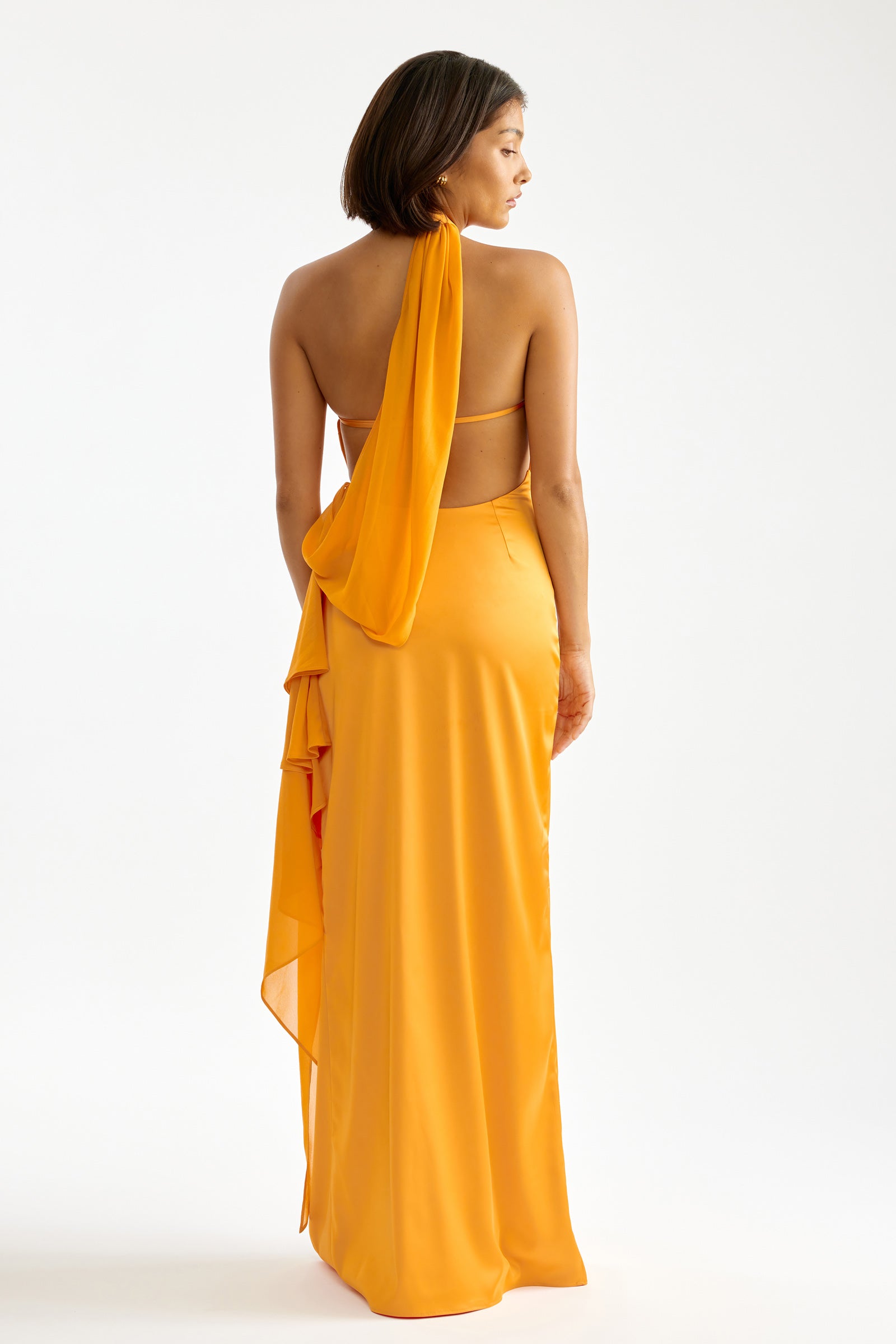 Mona Dress featuring a backless halter neck and flowing draped detail in vibrant orange for formal and wedding guest occasions by Studio Lexi