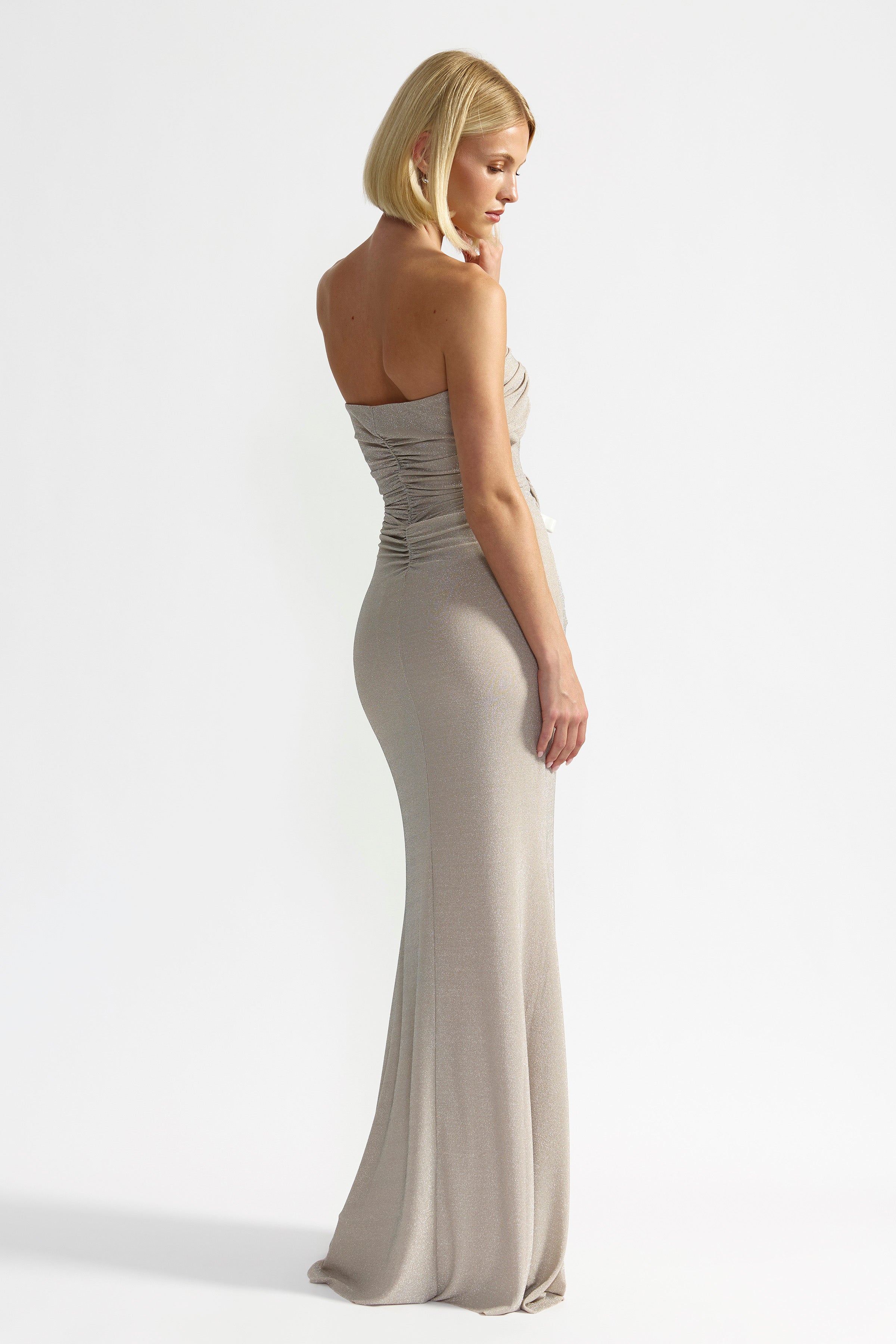 Tiffany Dress features a strapless backless silhouette with ruched detailing in champagne for formal and black tie occasions