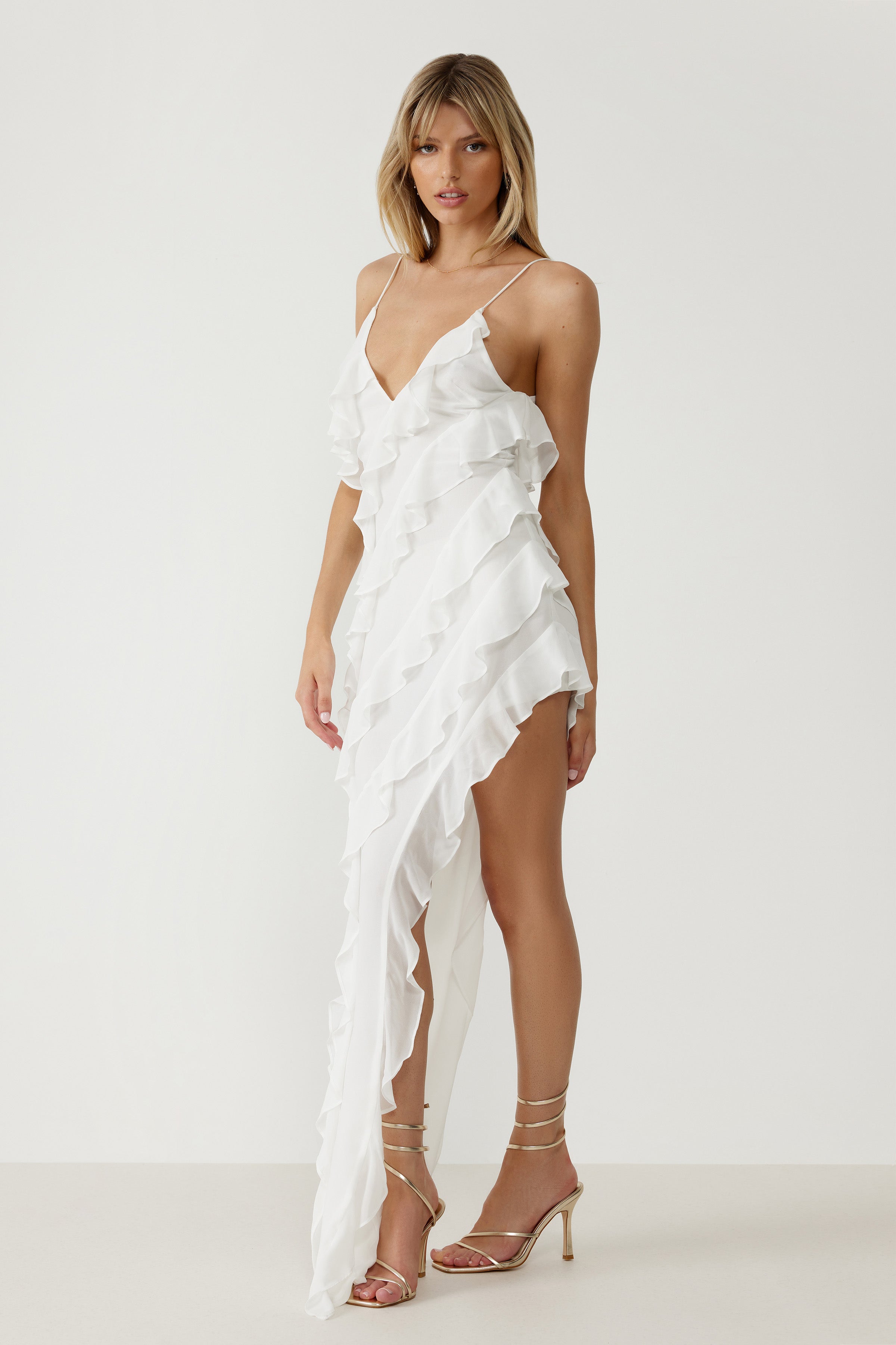 Etienne Dress featuring cascading ruffles, a deep V neckline, and high split in lightweight white fabric for formal events